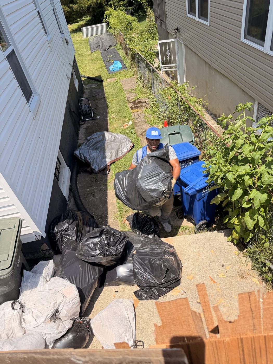 Crew carrying bagged junk out of a narrow side yard